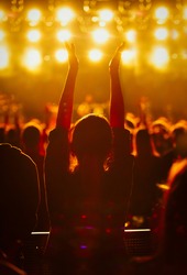 Silhouette of young girl waving hands to the music on popular dj concert in night club.Big group of people partying on electronic musical festival.Young woman have fun on nightclub party event