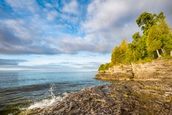 A small wave breaks and splashes under a cloudy blue sky at Door County, Wisconsin's Cave Point on the coast of Lake Michigan.