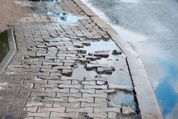 Puddle after rain on damaged paving slabs, dangerous pedestrian walkway. Pit with destroyed gray paving slabs on sidewalk, broken paving stones. Broken slab on pedestrian road