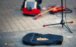 Street performers busking money. Street musician, guitar player make money. Guitar bag with coins and equipment of street musician in background. 