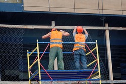 Workers team installing at height support chain-link fencing at construction site. Facade works