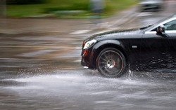 Car driving fast through big puddle at heavy rain, water splashing over the car. Car driving on asphalt road at heavy rain. Dangerous driving conditions. Dangers of aquaplaning. MOTION BLUR
