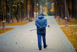Elderly man walking with walking cane in hand behind his back. Old man with cane enjoying walk in autumn city park. Senior man walk alone.