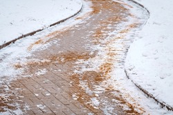 Sanding icy pedestrian sidewalk, maintenance of slippery surface in winter. Paving slabs sprinkled with salt and sand mixtures. De-icing chemicals on pavement. Prevent slipping on road with sand. 