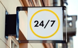 24 hours open sign or working around the clock sign hanging on wall. Working 24 hours, sign on facade of building.