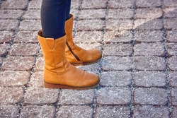 Woman feet in suede boots on salted pavement. Yellow suede shoes and salted pavement, road salt can ruin footwear. De-icing chemicals on paving slabs, female walking in leather boots in winter