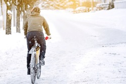 Cyclist rides on snow and snowdrifts in city during blizzard. Man in warm clothes wearing protective helmet riding on snowy slippery road on bicycle. Risk of cycling in winter. Winter cycling hazard