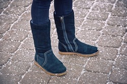 Woman legs in black boots stand on salty paving slabs. Salted sidewalk, paving slab covered with salt, road salt can damage shoes. Deicing chemicals on walkway, woman walking in boots in winter