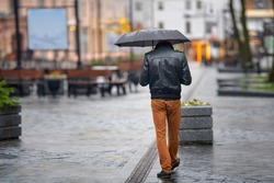 Man with umbrella walk on city street on rainy day. Alone man with umbrella. Back view of stylish man in rainy weather