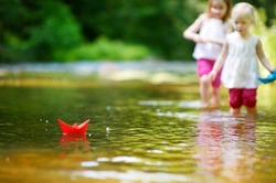 Two adorable little sisters playing with paper boats in a river