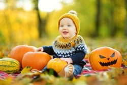 Cute small baby boy sitting near small pumpkin with painted scary face on sunny autumn day. Kid trick or treating on Halloween. Family time at Thanksgiving and Halloween. Festive season in October.