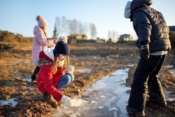 Group of children playing with thin ice puddles formed on the frozen soil in winter. Kids having fun in winter. Winter activities for kids.
