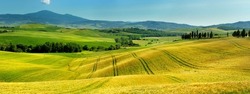 Stunning view of yellow fields and farmlands with small villages on the horizon. Summer rural landscape of rolling hills, curved roads and cypresses of Tuscany, Italy.