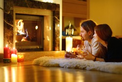 Happy couple having drinks by a fireplace in a cozy dark living room on Christmas eve