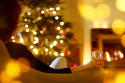 Woman having a drink by a fireplace in a cozy dark living room on Christmas eve