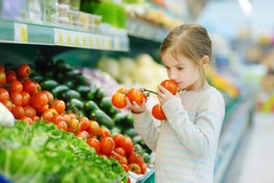 Little girl choosing tomatoes in a food store or a supermarket