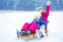 Two cute little sisters having fun with a sleight in beautiful winter park