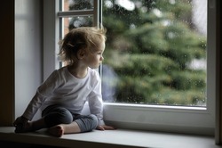 Adorable toddler girl looking at raindrops on the window