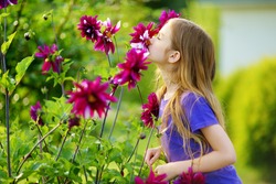 Adorable little girl sniffing purple flowers. Child and flowers, summer, nature and fun. Summer holidays.