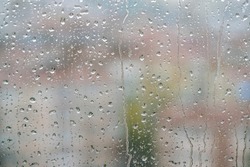 rain, raindrops on windowpane over blurred city view. Rain drops on window against blur background  or surface with buildings or houses while raining with selective focus and noise effects