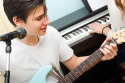 Teenage boy playing electric guitar and singing while girl plays on piano.
