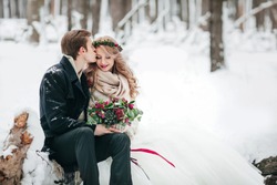 Groom is kissing his bride on the temple on background of the snowy forest. Winter wedding. Artwork. Copy space