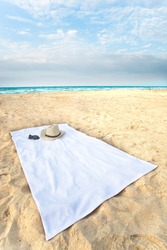 Wide angle towel on the beach, with hat and sunglasses.