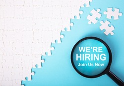 White jigsaw puzzle with word we're hiring over blue background. Recruitment Concept