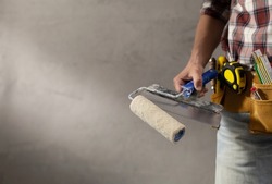 Construction worker man holding paint roller tool in house room renovation. Male hand and construction tools near concrete or plaster wall. Home renovation concept