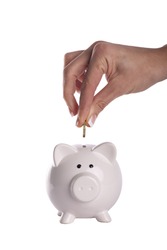 Hand putting money in a piggy bank, white background.