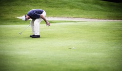 Golf player convulsed with laughter after ball just missed hole.