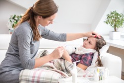 mother sits at the bedside of the sick daughter  and measures the temperature