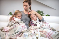 mother sits on the couch with 2 sick daughters and measures the temperature