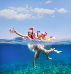 happy family with children is swimming and having fun in the sea in santa hat. Christmas holiday.