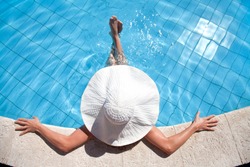 Unrecognizable woman in big hat relaxing on the swimming pool