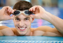 Happy smiling athletic swimmer wearing glasses at swimming pool