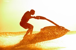 strong man jumps on the jetski above the water at sunset .silluet. spray.