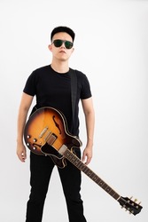 Young asian guy guitarist standing over isolated white background with a sunburst brown semi hollow body strapped to the front
