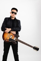 Young asian guy guitarist standing over isolated white background with a sunburst brown semi hollow body arms folded wearing jacket