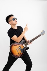 Young asian guy guitarist standing over isolated white background with a sunburst brown semi hollow body pointing top right