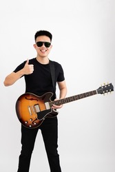 Young asian guy guitarist standing over isolated white background with a sunburst brown semi hollow body with thumbs up smiling expressiong