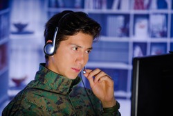 Portrait of handsome young soldier wearing a military uniform, military drone operator watching at his computer and using his headphone to give an advice