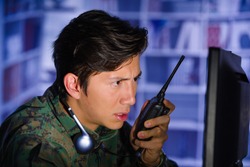 Portrait of young soldier wearing a military uniform, military drone operator watching at his computer and using a radio to give an advice, with headphones around his neck