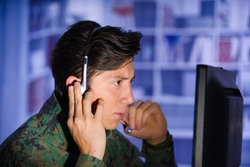 Portrait of handsome soldier wearing a military uniform watching important information in his computer, with one hand in the headphones and giving an advice in a blurred background, profile picture