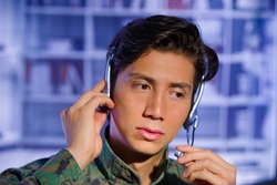 Portrait of handsome soldier wearing a military uniform, watching at his computer and fixing his headphones around the head, ready to give an advice, in a blurred background