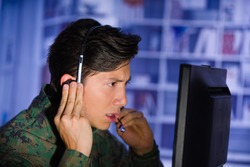Portrait of handsome soldier wearing a military uniform watching important information in his computer, with one hand in the headphones and giving an advice in a blurred background, profile picture