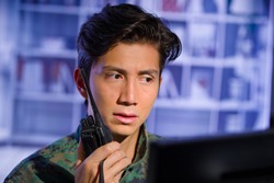 Portrait of worried young soldier wearing a military uniform, military drone operator watching at his computer and using a radio to give an advice