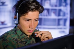 Portrait of soldier wearing a military uniform, operating at his computer and talking through his headphones during a military operation, in a blurred background