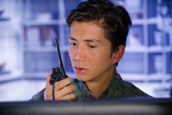 Portrait of young soldier wearing a military uniform, military drone operator watching at his computer and using a radio to give an advice