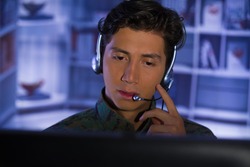 Portrait of young soldier wearing a military uniform, military drone operator watching at his computer and talking through his headphones to give an advice